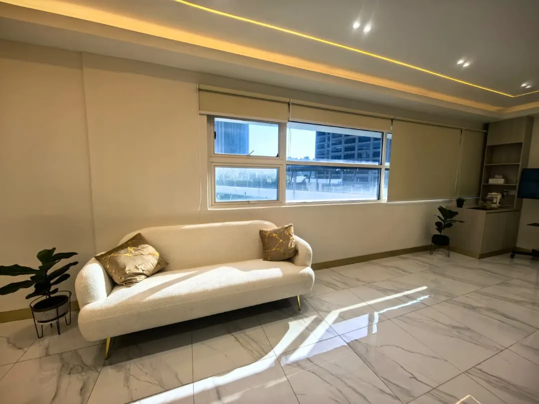 Bright living room with white sofa, large windows, and marble floors. Modern home interior.