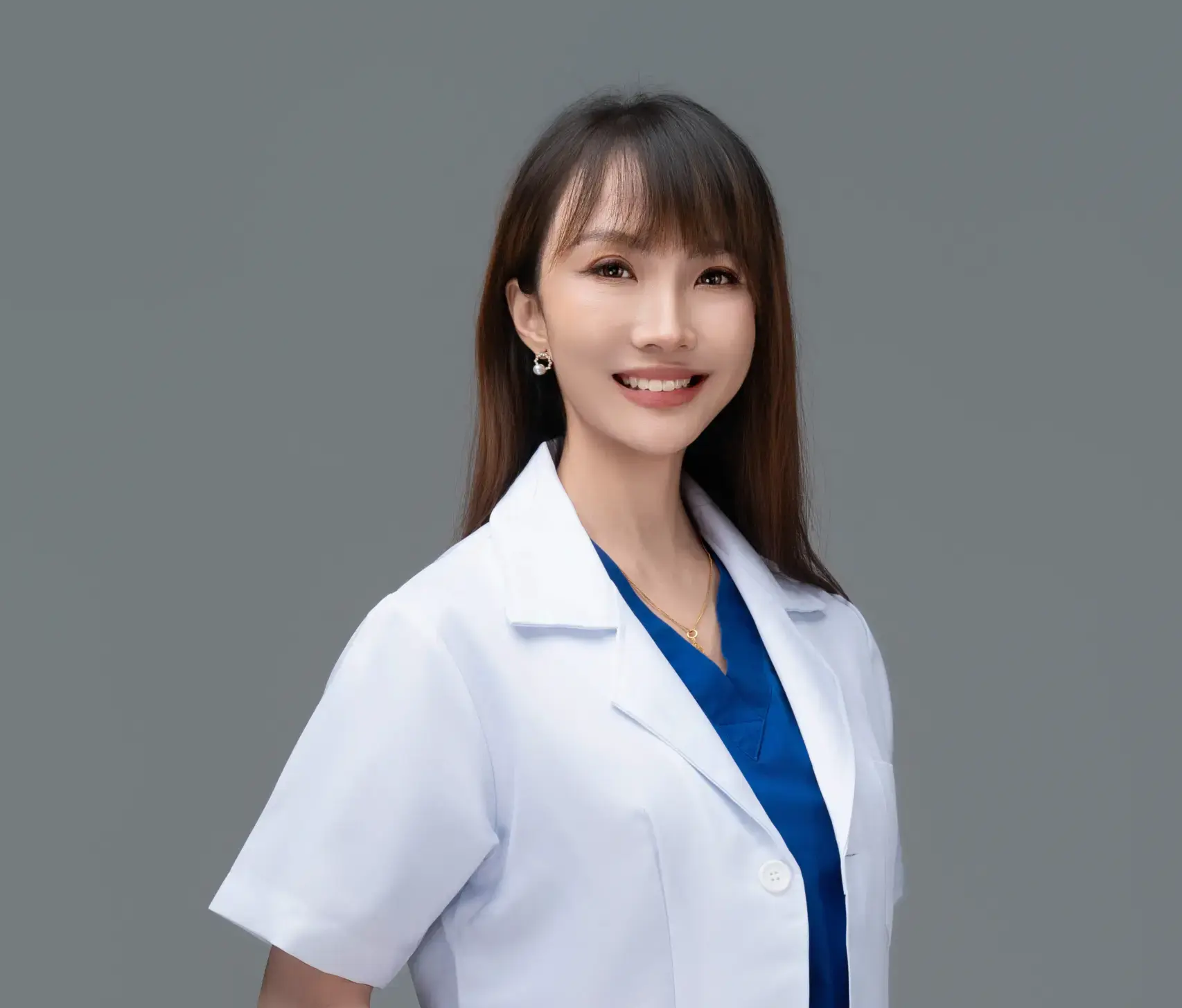 Smiling Asian female doctor in a white lab coat and blue scrubs.
