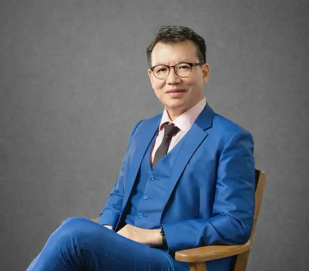 Man in blue suit sitting in chair, looking at camera.